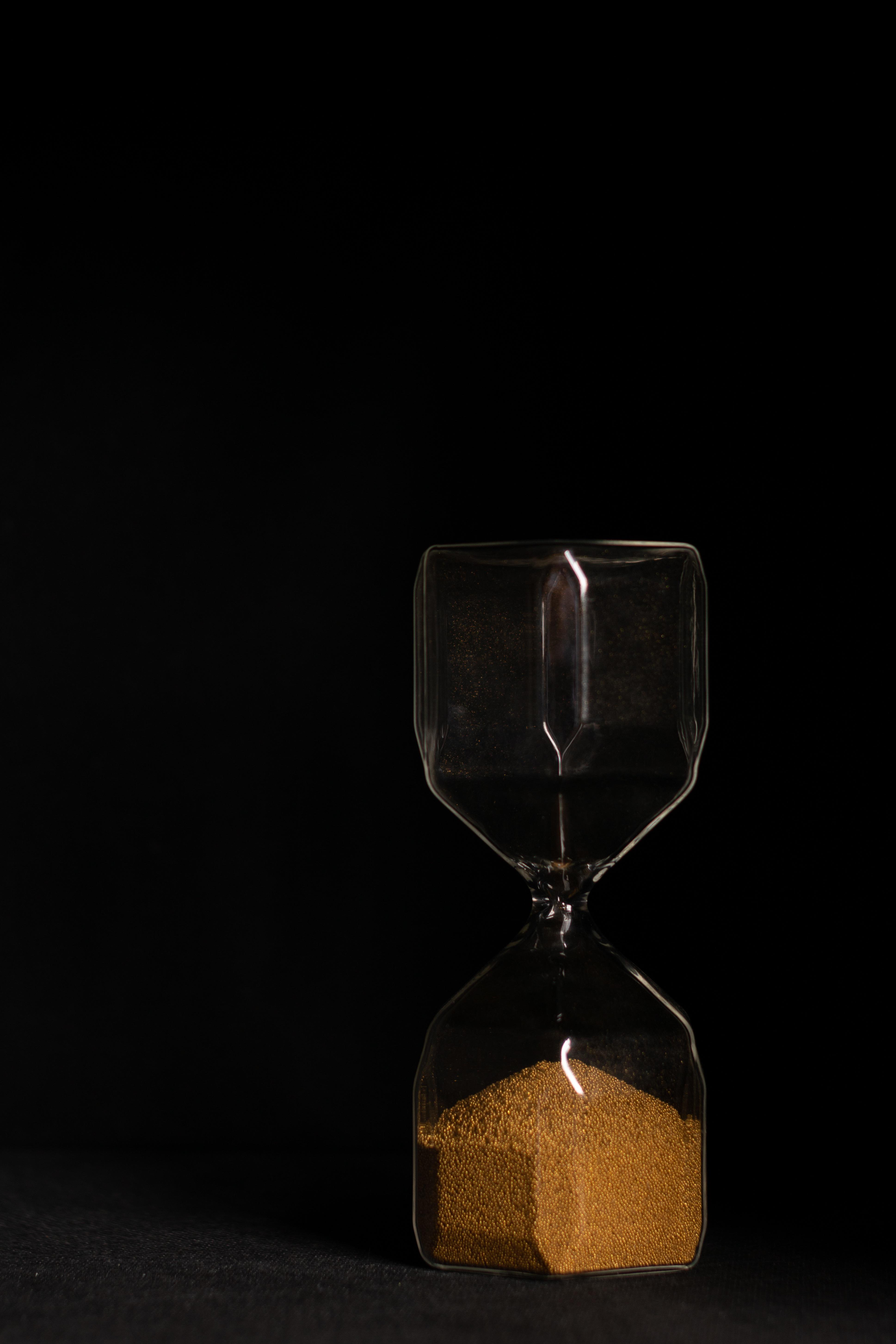 A glass hourglass holding golden sand against a dark background.